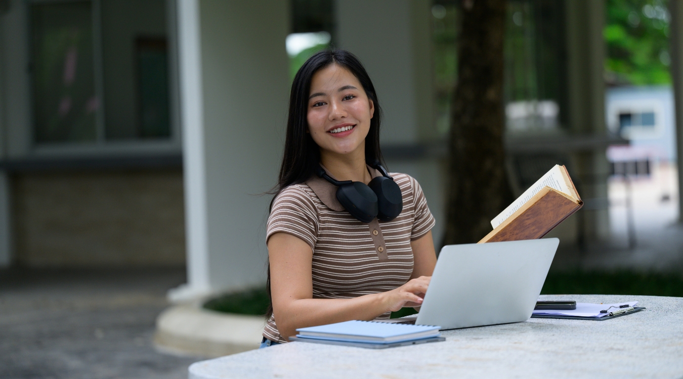 Filipina content writer working alfresco outdoors with laptop and books improving content writing skills while looking at camera