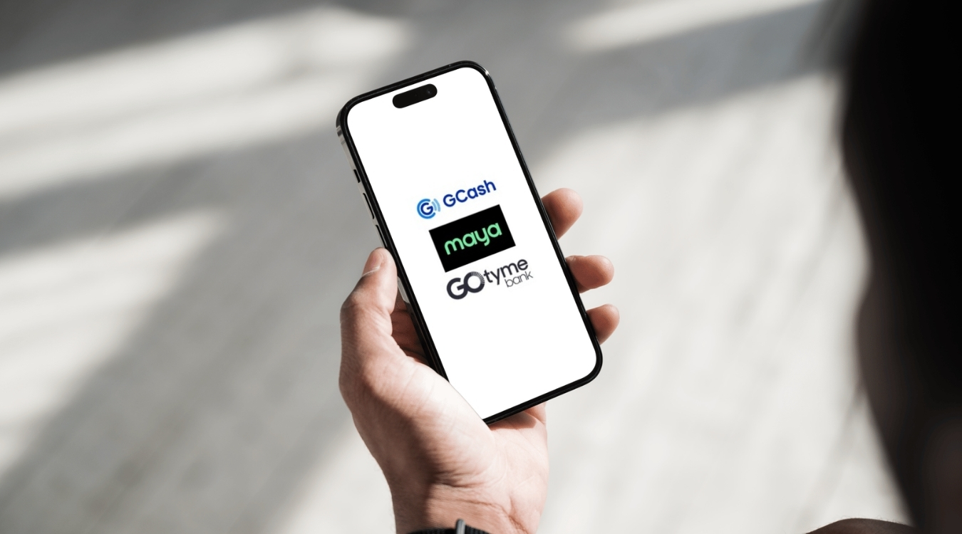 Filipino freelancer holding smartphone showing GCash Maya and GoTyme e-wallet app logos on screen for comparison