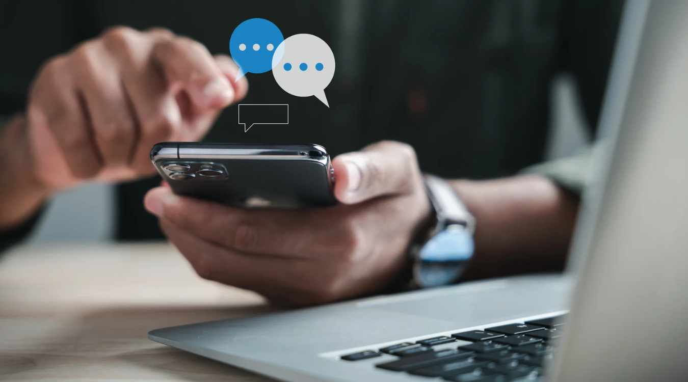 Filipino freelancer hand using smartphone with chat thread icon floating above while laptop sits in the foreground
